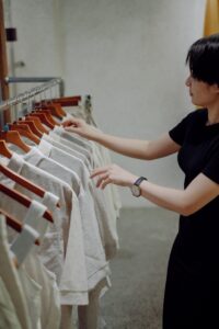 a woman in a black dress looking at a rack of white shirts